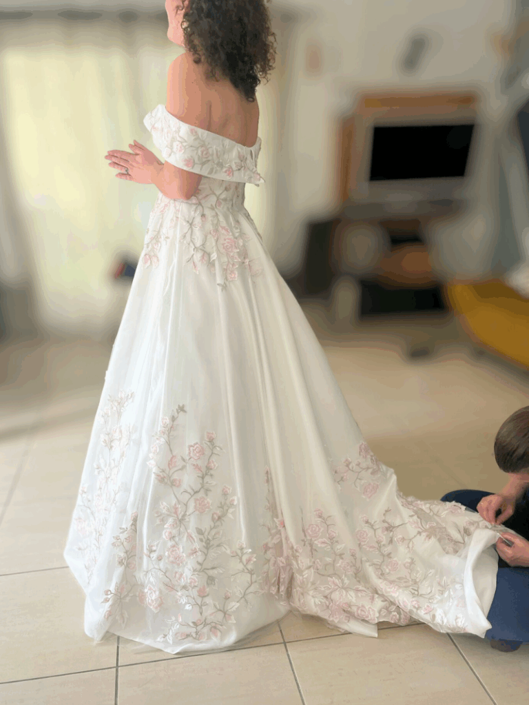 Essayage de la robe col bardot par la future mariée – harmonie des teintes pastel et de la silhouette princesse.